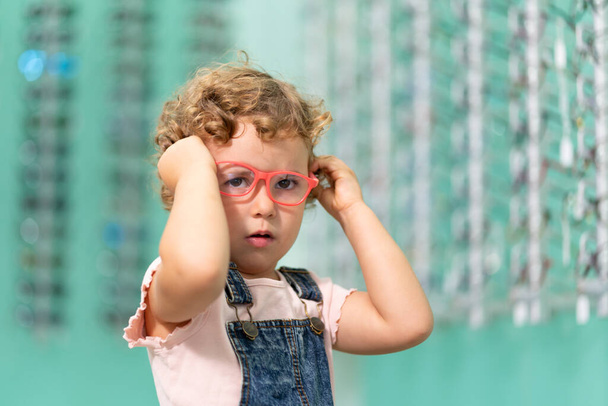 Egy szőke kislány szemüveget próbál fel egy optikus boltban.. - Fotó, kép