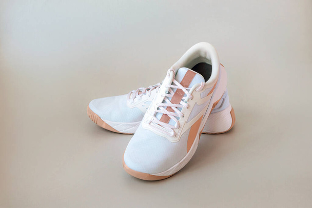 Bílé tenisky s béžovými pruhy na světle neutrálním pozadí. Sportovní boty stylové ženy. Sportovní a fitness koncept. - Fotografie, Obrázek