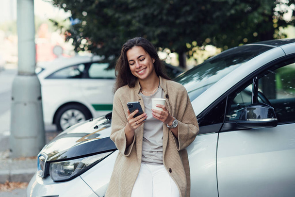 Fiatal csinos nő csésze kávé és SMS blog tabletta őszi parkban jármű közelében - Fotó, kép