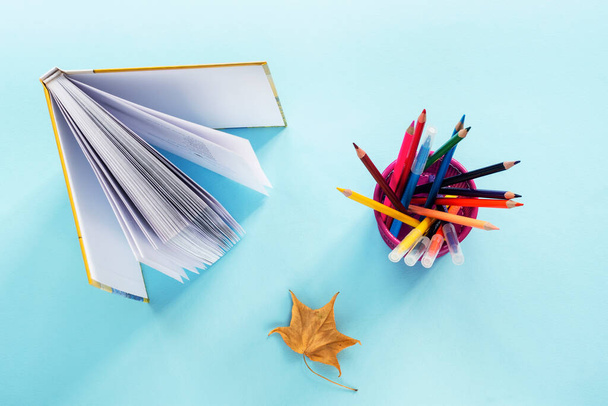 Σχολικές προμήθειες, ανοιχτό βιβλίο και κίτρινο φύλλο σε μπλε φόντο. Πάνω άποψη, επίπεδη lay. Επιστροφή στο σχολείο έννοια. - Φωτογραφία, εικόνα