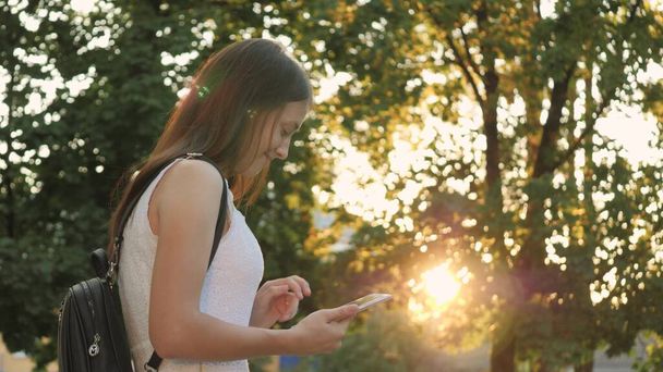 Ein Mädchen studiert in einem Tablet in den Sonnenstrahlen der Stadt, erledigt Online-Einkäufe bei Sonnenuntergang in einem Online-Shop, checkt E-Mails in sozialen Netzwerken, chattet, liest Bücher und Nachrichten in Informationsquellen von Websites - Foto, Bild