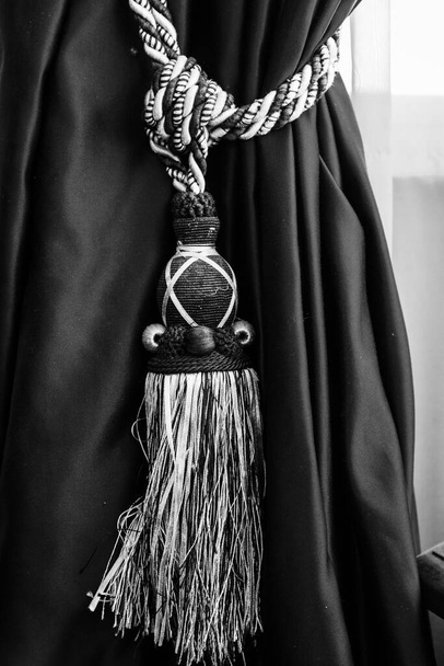 fechar de uma cortina elegante amarrado com uma corda decorativa e um acessório franjado, detalhe do tecido, estilo e decoração em preto e branco - Foto, Imagem
