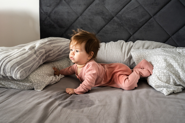 Small caucasian baby lying down on the belly on the bed with wet urine stain on the sheet and clothes looking to the side Bedwetting child pee on the bed - Foto, afbeelding