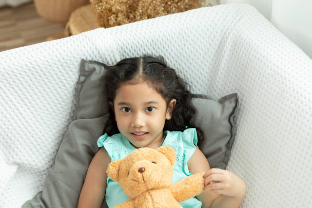 the innocences thai little girl sleeping playing teddy bear on white sofa at home - Photo, Image