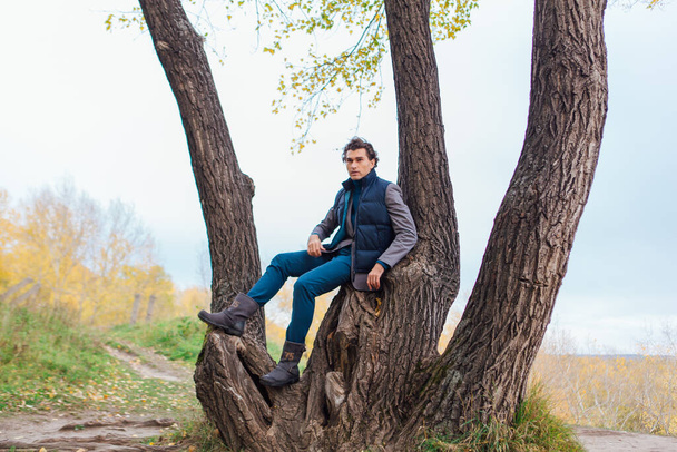 Tall handsome man climbing on the tree in yellow autumn forest - Valokuva, kuva
