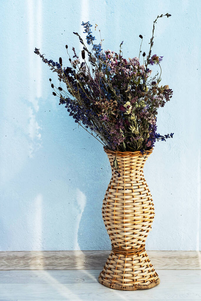 Gedroogde bloemen in rieten vaas tegen blauwe muur. Home eco decor, kopieerruimte. - Foto, afbeelding