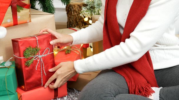 Close up woman hands wrap present gift in cozy living room. Woman wrapping christmas gift box under xmas tree. Asian woman decor bauble ball christmas tree in xmas holiday winter seasonal celebration - Foto, Imagen