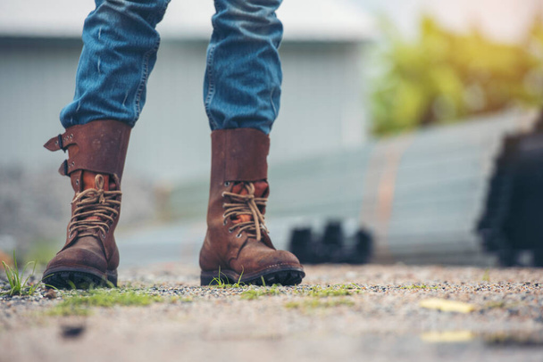 男性は建設現場で労働者のための安全靴をブーツを着用します。エンジニアは、精製所を背景にジーンズブラウンブーツワーカーを着用してください。エンジニア安全産業ファッション履物屋外を歩く - 写真・画像