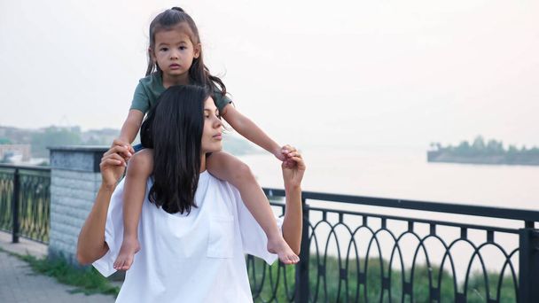 Frau trägt barfüßige Tochter auf Schultern über Böschung - Foto, Bild