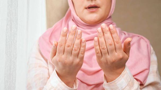Tuntematon nainen vaaleanpunaisessa hijabissa lukee rukouksen kädestä hänen edessään ja pesee kasvot - Valokuva, kuva