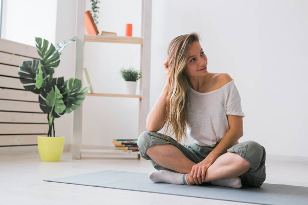 Positive girl sitting on fitness mat resting after pilates or yoga practice. Mindfulness and wellbeing concept. - Фото, изображение