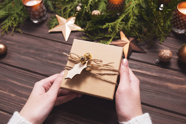 Christmas gift in female hands on a wooden background. - Photo, Image