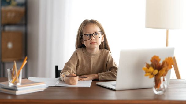 Back to school. Thinking child is sitting at desk. Girl doing homework or online education. - 写真・画像