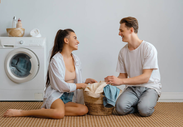 Beautiful young loving couple is smiling while doing laundry at home. - Foto, imagen