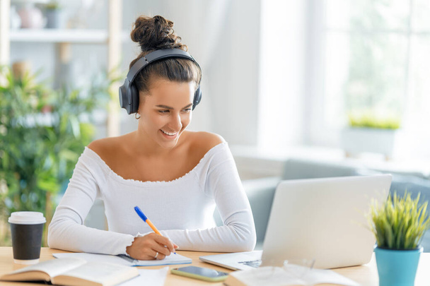 Focused young businesswoman studying online, watching webinar, podcast on laptop, making notes, sitting at work desk. E-learning concept. - Фото, изображение