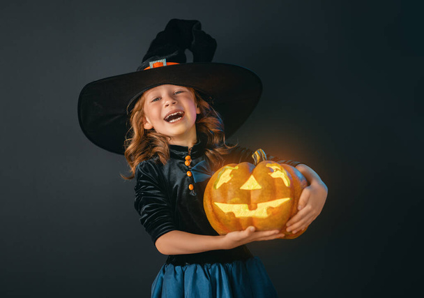 Happy Halloween! Cute little laughing girl in witch costume on black wall background.  - Fotó, kép