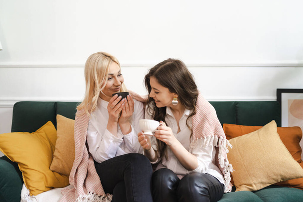 Mother with daughter drinking tea together in living room at home - Photo, image