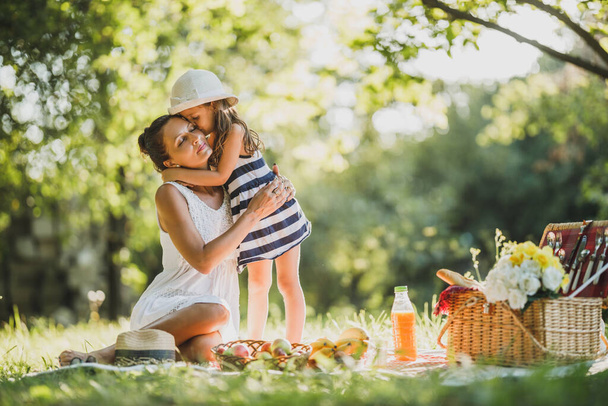 Симпатична маленька дівчинка обіймає і цілує свою красиву маму, насолоджуючись днем пікніка в природі
. - Фото, зображення