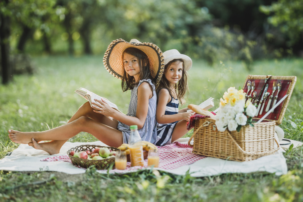 Kaksi söpöä hymyilevää sisarta lukemassa kirjoja luonnossa ja nauttimassa piknikpäivästä. Katson kameraa.. - Valokuva, kuva