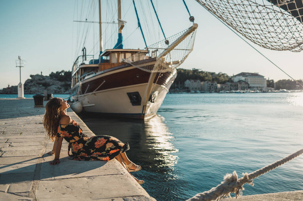 Μια ελκυστική νεαρή γυναίκα που κάθεται στην υπέροχη παραλία της Μεσογείου και απολαμβάνει τις καλοκαιρινές διακοπές. - Φωτογραφία, εικόνα