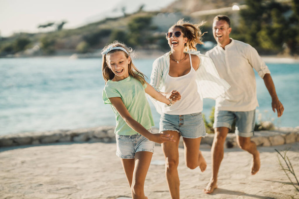 夏休みを楽しみながら海の近くを歩いている笑顔の10代の少女と彼女の両親. - 写真・画像
