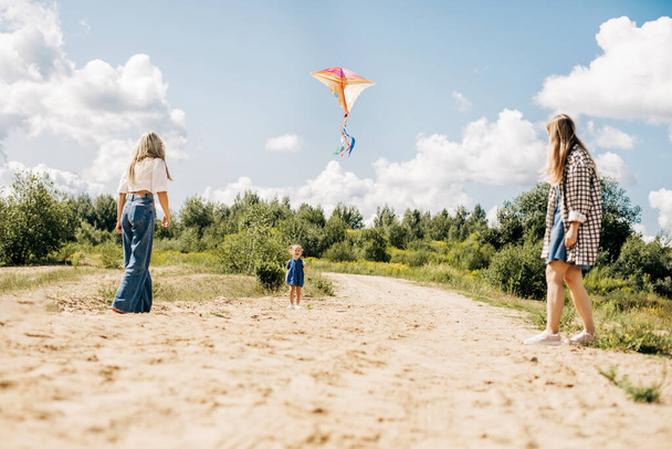 Una madre vuela una cometa con sus hijas durante unas vacaciones familiares en el campo - Foto, imagen