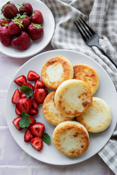 Cottage cheese pancakes, ricotta fritters on ceramic plate with  fresh strawberry. Healthy and delicious morning breakfast.  Grey concrete background. - Photo, Image