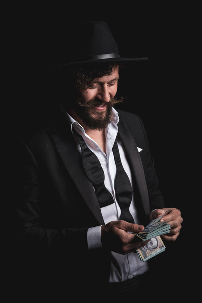 feliz hombre de negocios está contando su dinero rumano y usando un sombrero sobre fondo negro - Foto, imagen