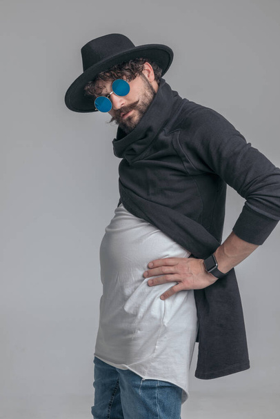 guapo hombre casual flexionando su vientre y siendo despreocupado contra gris fondo de estudio - Foto, Imagen