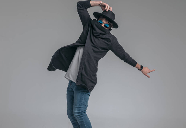 fashion model verbergen zijn gezicht in zijn vest kraag, het aanpassen van zijn hoed en poseren met houding  - Foto, afbeelding
