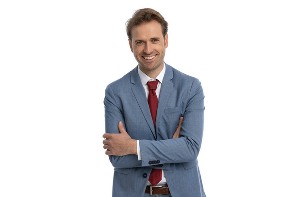 happy elegant businessman in suit crossing arms and smiling while posing on white background in studio, portrait - Photo, Image