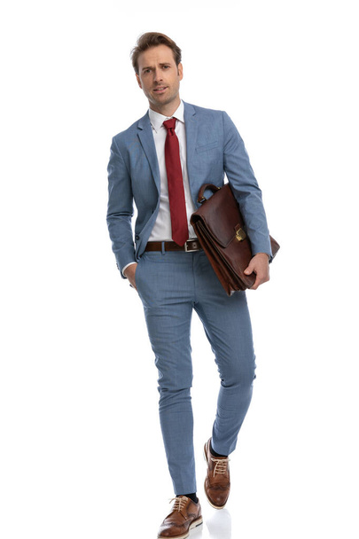 zelfverzekerde zakenman in blauw pak hand in hand, koffer vasthouden en geïsoleerd lopen op een witte achtergrond in de studio - Foto, afbeelding
