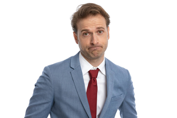 portrait of elegant young guy in blue suit making a disappointed face and posing in front of white background in studio - Foto, Imagen