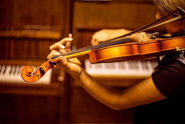 νεαρός βιολιστής παίζει μουσική στο βιολί με την πλάτη του κοντά στο πιάνο, horizonta - Φωτογραφία, εικόνα