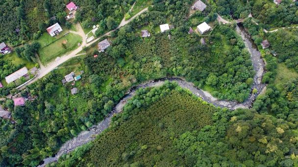 Légi drón kilátás a természet Grúziában. Völgy keskeny folyó és falu, dombok lejtők borított zöld, függőleges kilátás - Fotó, kép
