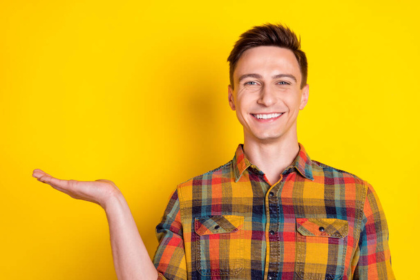 Portrait of attractive cheerful guy holding on palm copy blank place space ad isolated over bright yellow color background - Photo, image