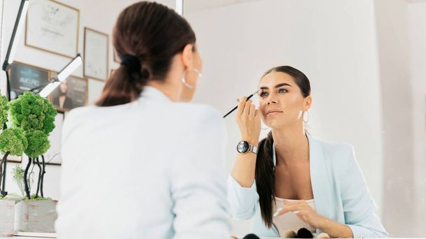 Woman paints her eyebrows looking into a mirror in a beauty salon - Фото, зображення