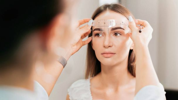 Make-up master comprueba las cejas del cliente usando una regla de cejas - Foto, imagen