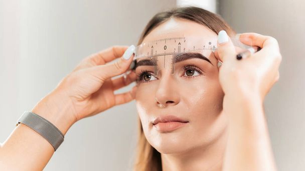 Make-up-Meister überprüft die Augenbrauen der Kundin mit einem Augenbrauenlineal - Foto, Bild