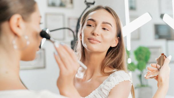 Χαμογελώντας make-up master κάνει μακιγιάζ για έναν πελάτη. Ζωγραφική δέρματος - Φωτογραφία, εικόνα