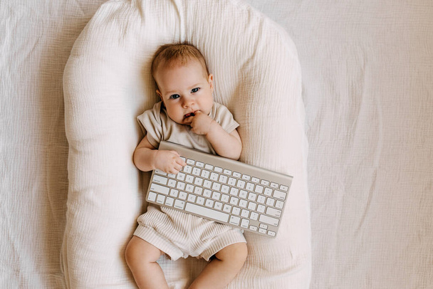 Baby lying in a baby nest, holding a keyboard. - 写真・画像