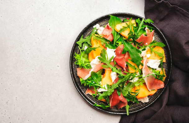 Melon salad with cantaloupe, prosciutto, goat cheese and arugula on white background, top view, copy space - Photo, image