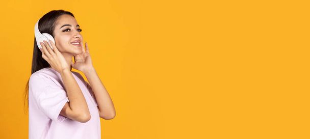 Side view portrait of young beautiful woman in headhones isolated over yellow background - Fotoğraf, Görsel