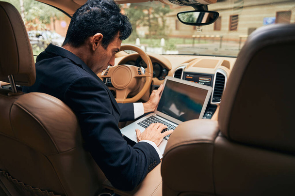 Stylish businessman working on laptop inside a car - Valokuva, kuva