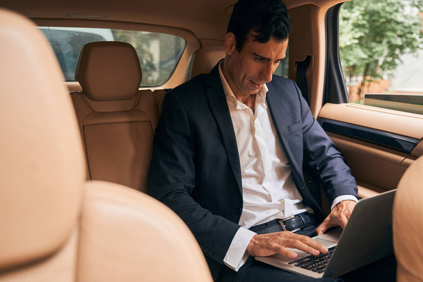 Focused businessperson typing on laptop keyboard from car - Foto, Bild
