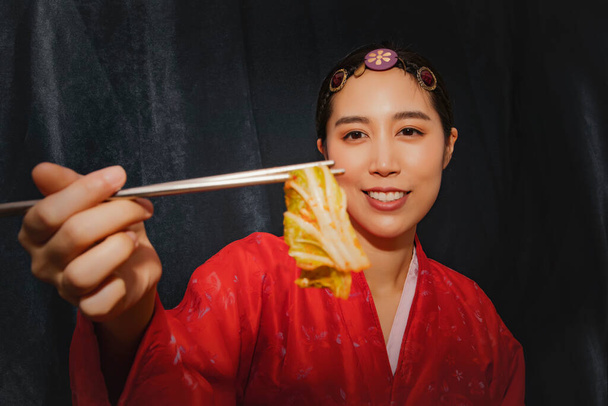 Dispara impresionante retrato de una mujer que usa hanbok coreano rojo mira la deliciosa col blanca tradicional, pepinillos, kimchi: las mujeres asiáticas se enorgullecen de la col china, receta casera de kimchi. - Foto, Imagen