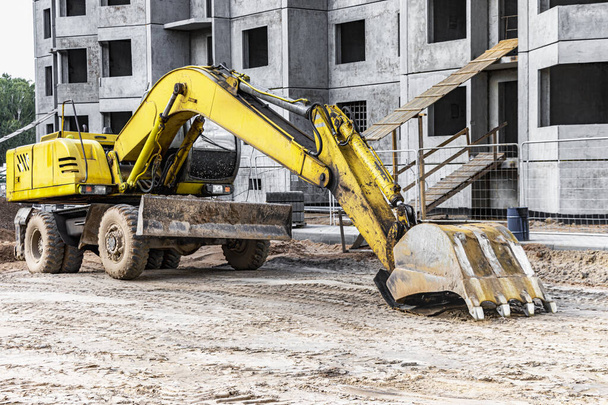 A heavy crawler excavator with a large bucket is getting ready for work in front of a panel house under construction .. Heavy construction equipment for earthworks. Quarry excavator - Фото, зображення