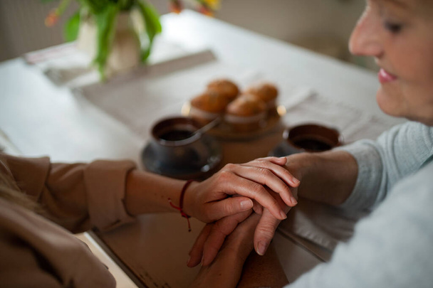 Close up of senior mother holding hands with adult daughter indoors at home, having coffee. - Fotografie, Obrázek