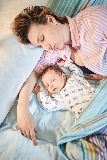 Портрет новорожденного ребенка и матери, спящей на кровати, отдыхающей вместе
 - Фото, изображение
