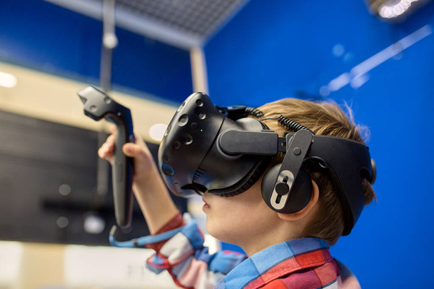 современные технологии, игры и концепция людей - мальчик в гарнитуре виртуальной реальности или 3D очки, играющий в видеоигру в игровом центре
 - Фото, изображение